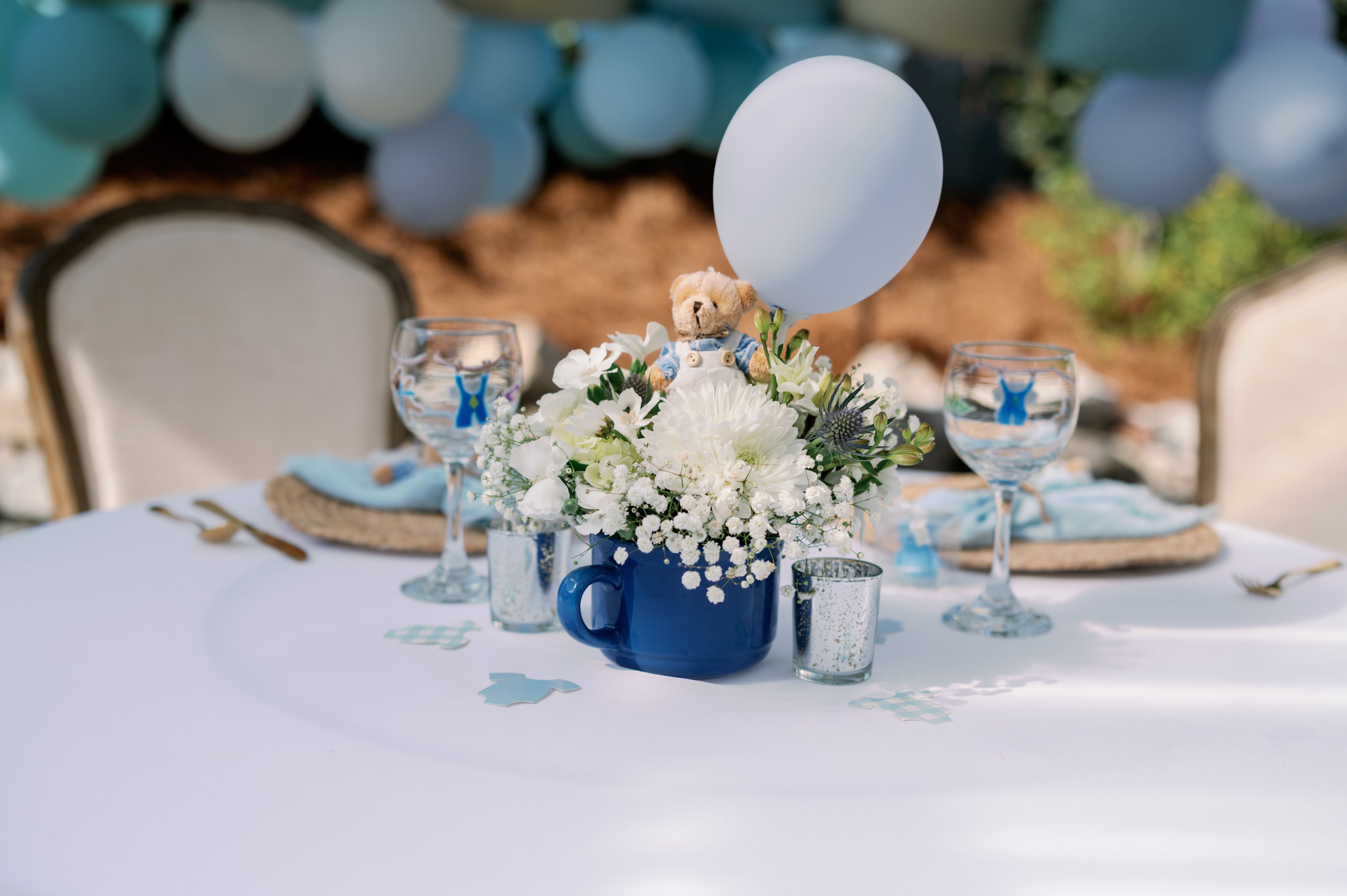 Baby shower table setting with blue and white floral centerpiece, teddy bear, and balloon accents in the Canal Street Inn garden
