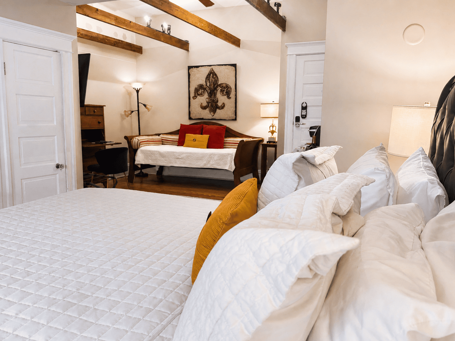 The Fleur-de-lis Room — king bed, daybed with red pillows, fleur-de-lis art, and exposed wood beams