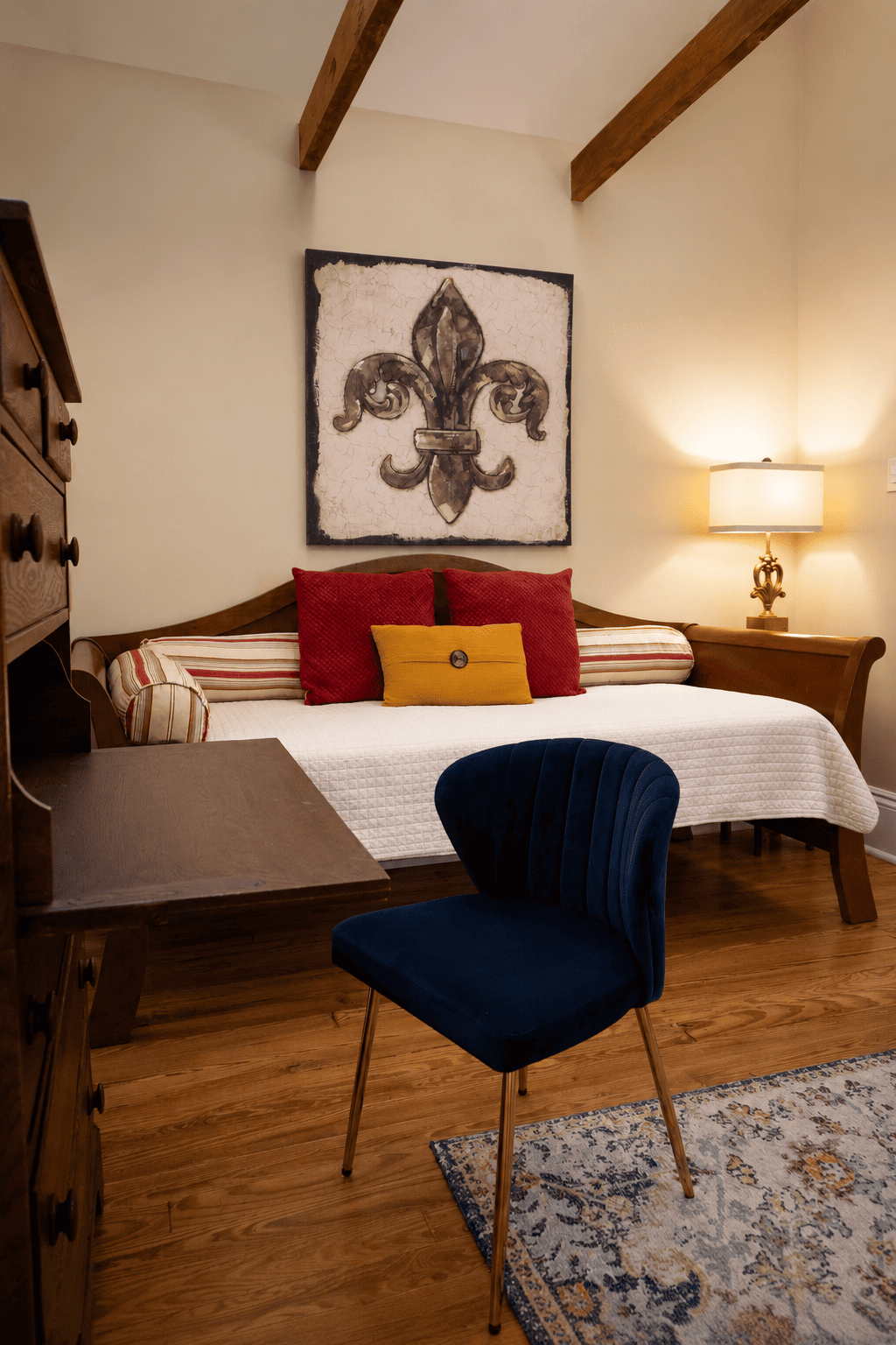 The Fleur-de-lis Room — daybed with red and yellow pillows, fleur-de-lis wall art, navy velvet chair, and writing desk