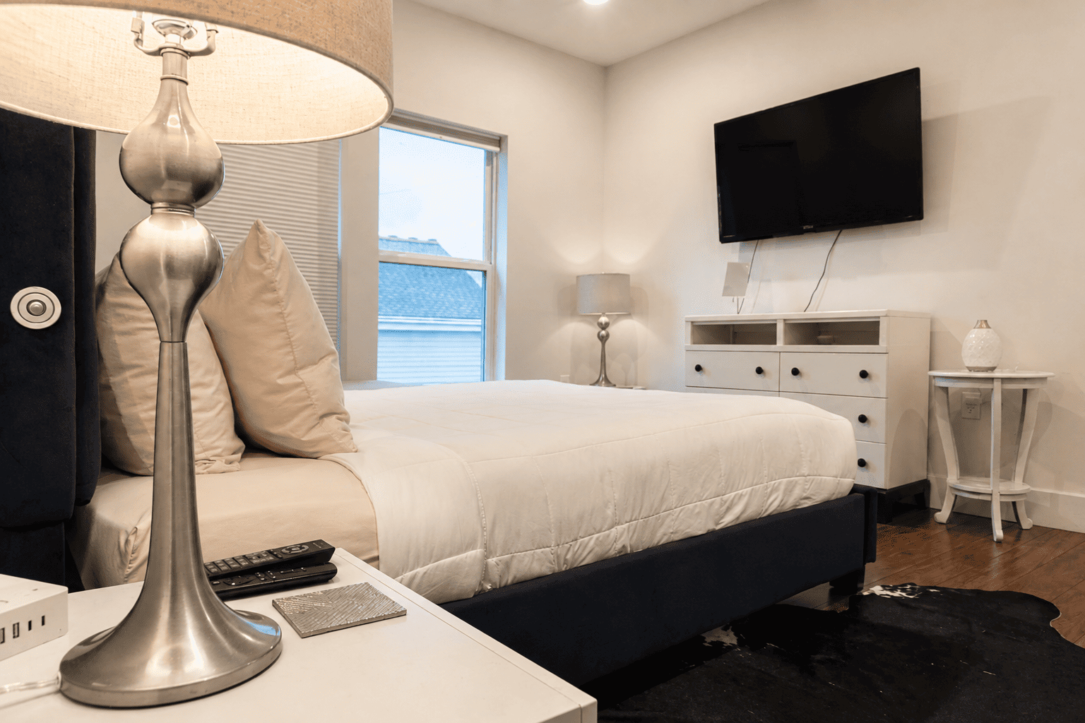 Second Floor Garden View Apartment — bedroom with white bedding, dresser with wall-mounted TV, and cowhide rug