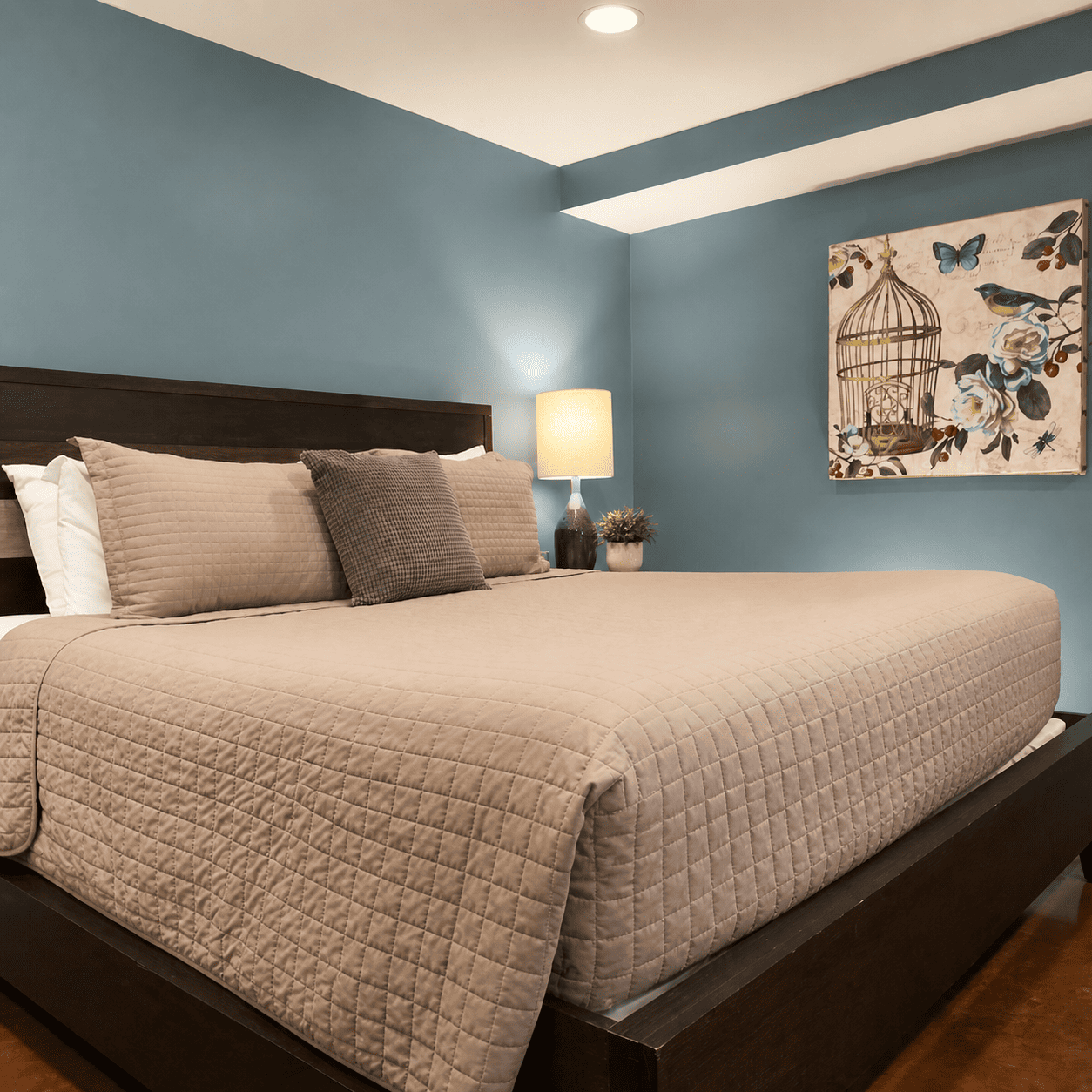 The Jasmine Room — king bed with quilted coverlet, dusty blue walls, and warm bedside lamp