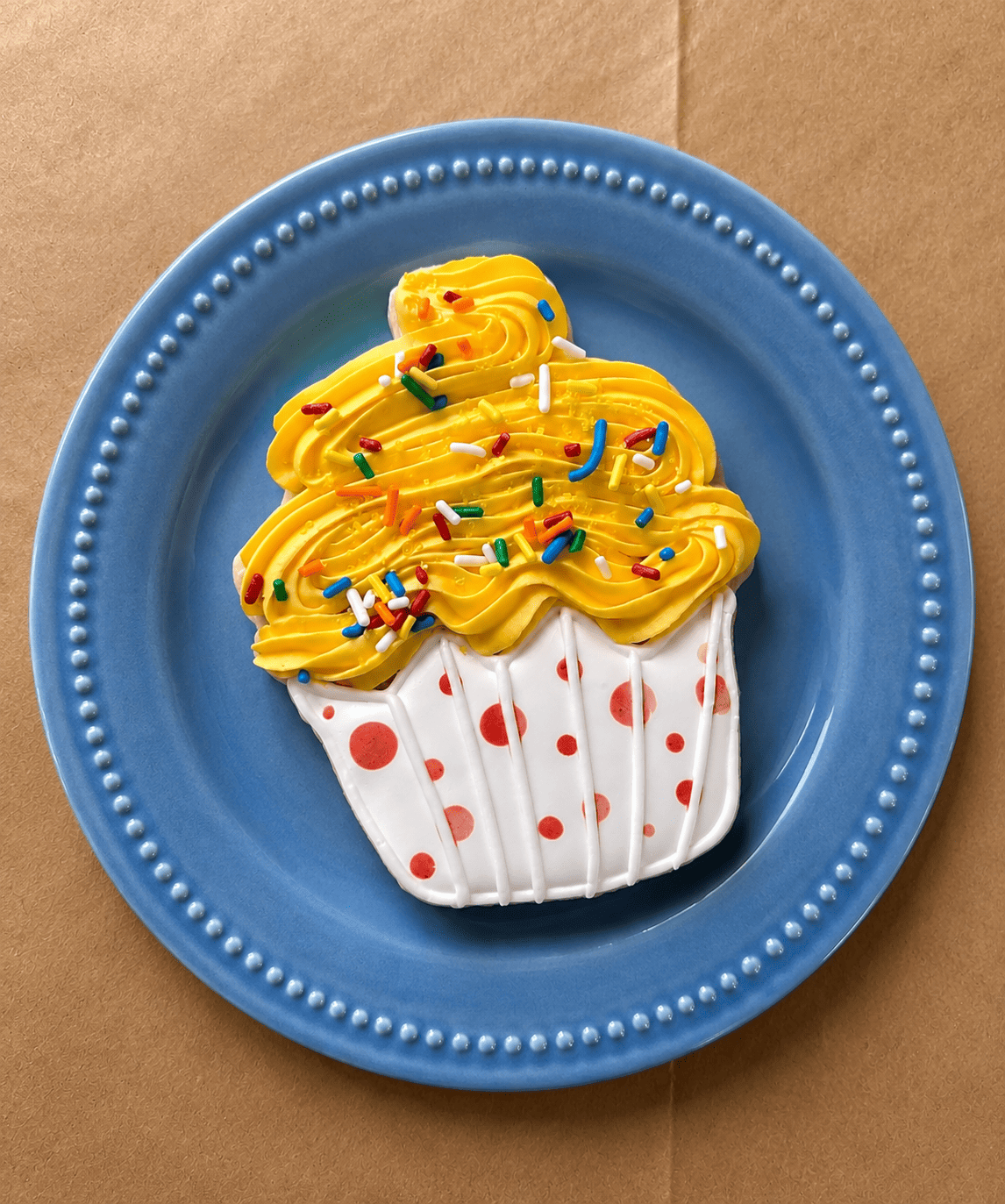 Cupcake-shaped sugar cookie with yellow swirl icing, sprinkles, and a red-polka-dot liner