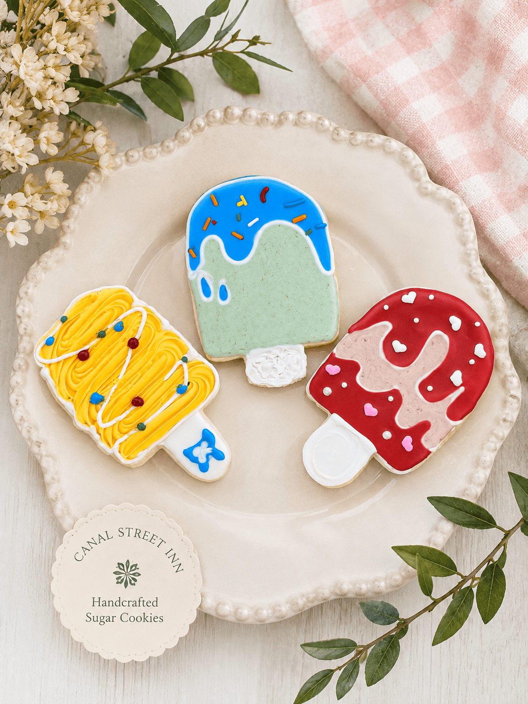 Canal Street Inn handcrafted popsicle cookies on a beaded cream plate with the inn seal