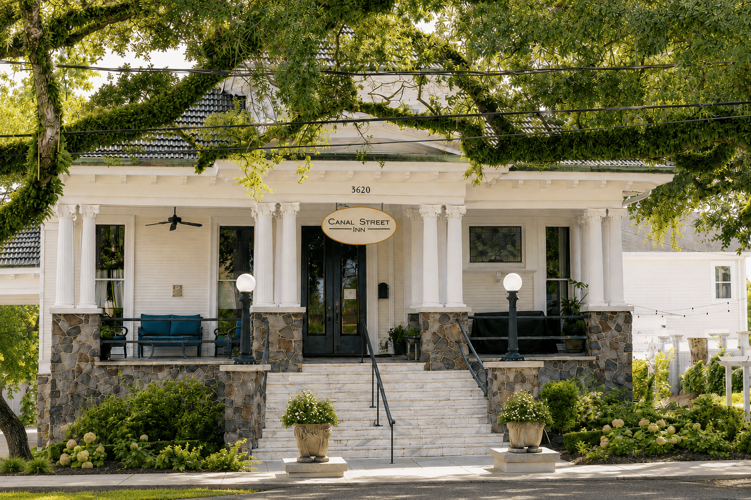 Canal Street Inn front porch with fluted columns, stone base, and hanging oval sign under live oaks