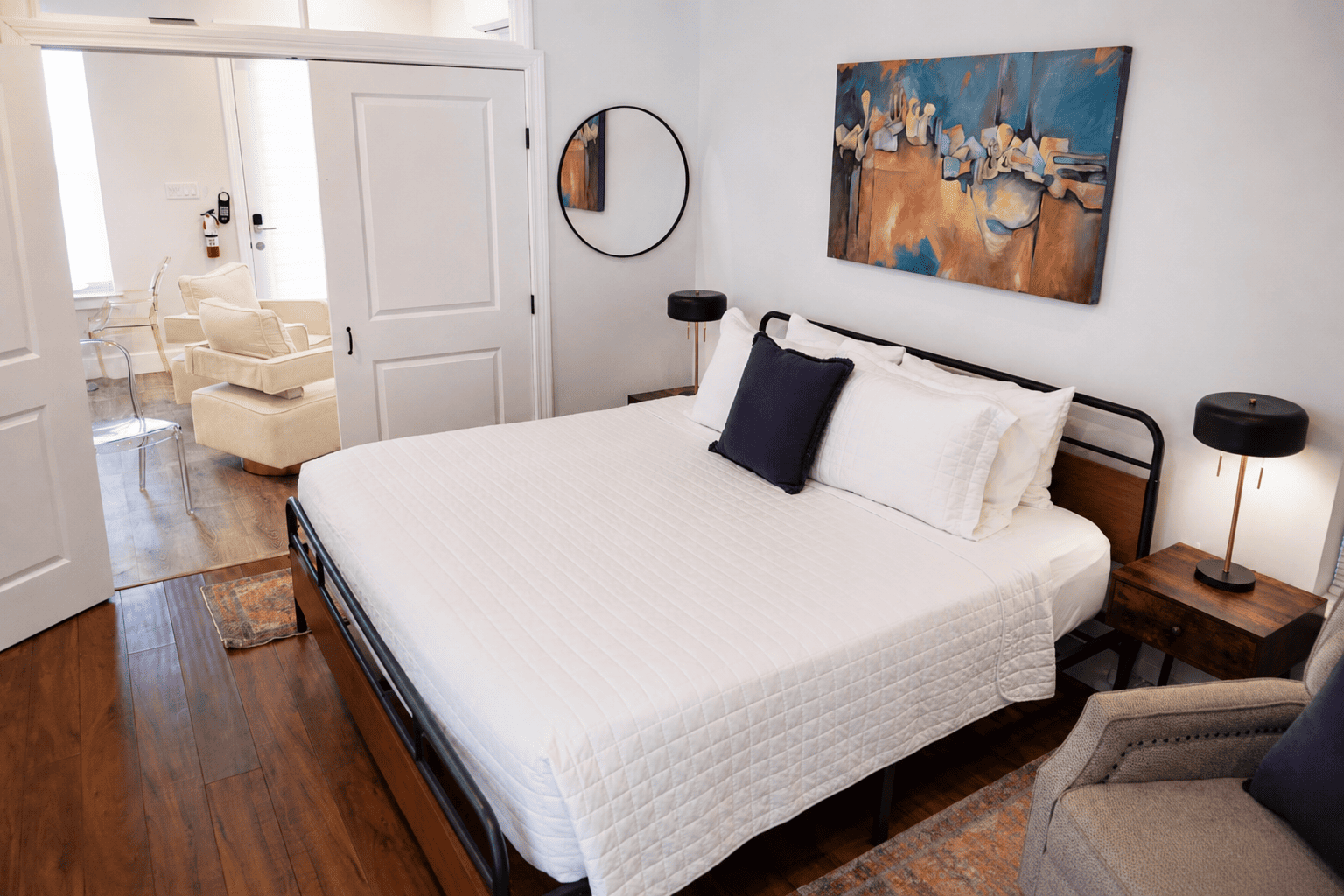 Petite Garden Suite — king bed with white quilted bedding, abstract painting, and open doors to the sitting area