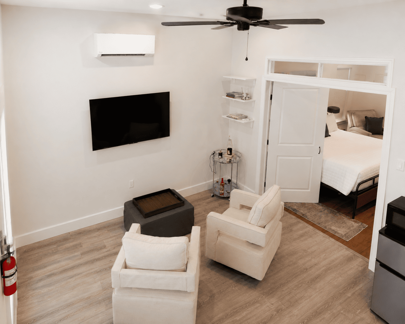 Petite Garden Suite — living area with armchairs, ottoman, wall-mounted TV, and view into the bedroom
