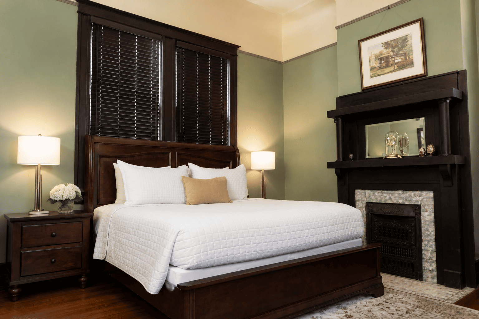 The Prytania Suite — king bed with sage walls, mahogany nightstands, and ornate fireplace mantel