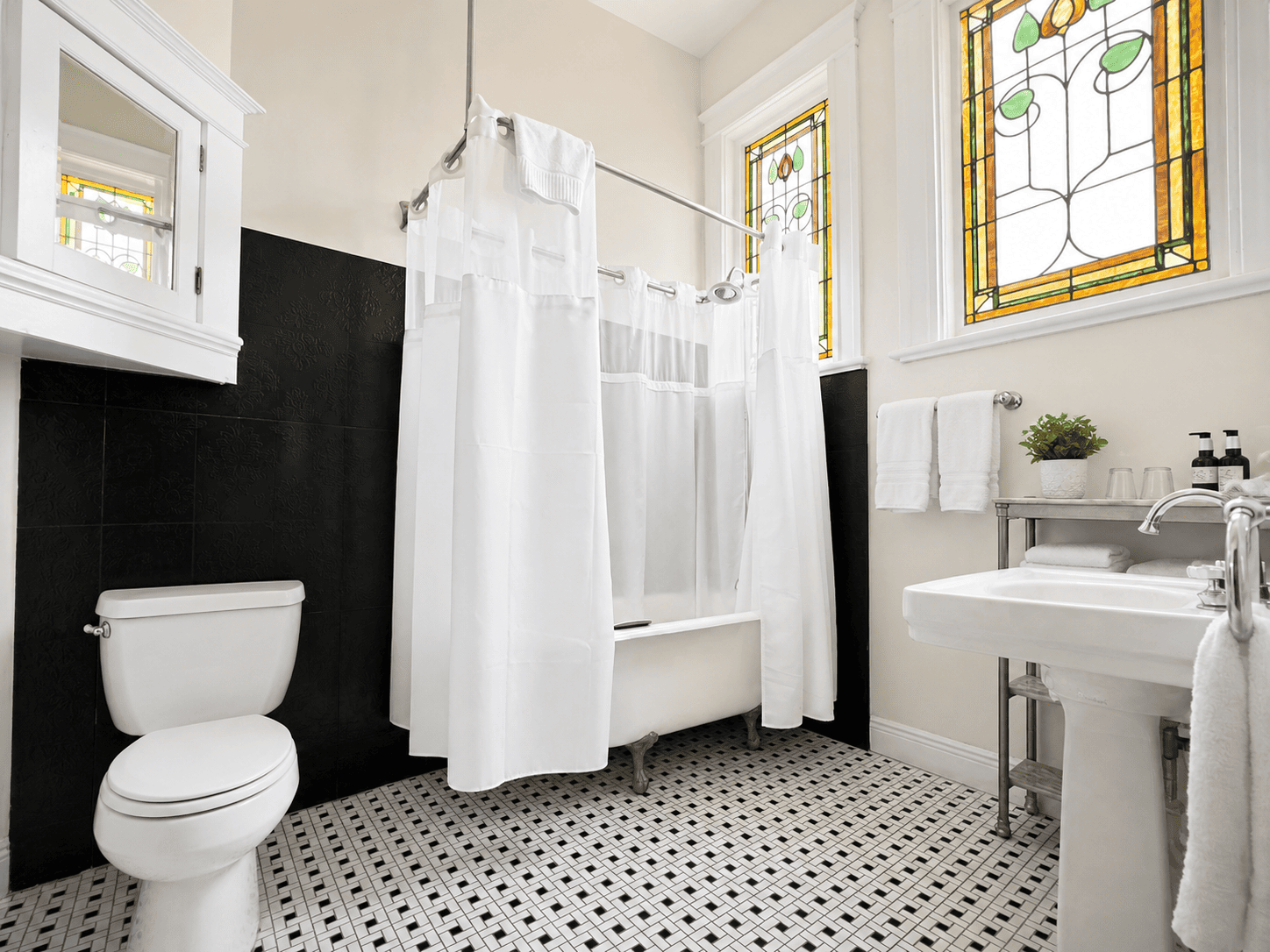 The Royal Street Room — bathroom with antique claw-foot tub, pedestal sink, and stained-glass windows