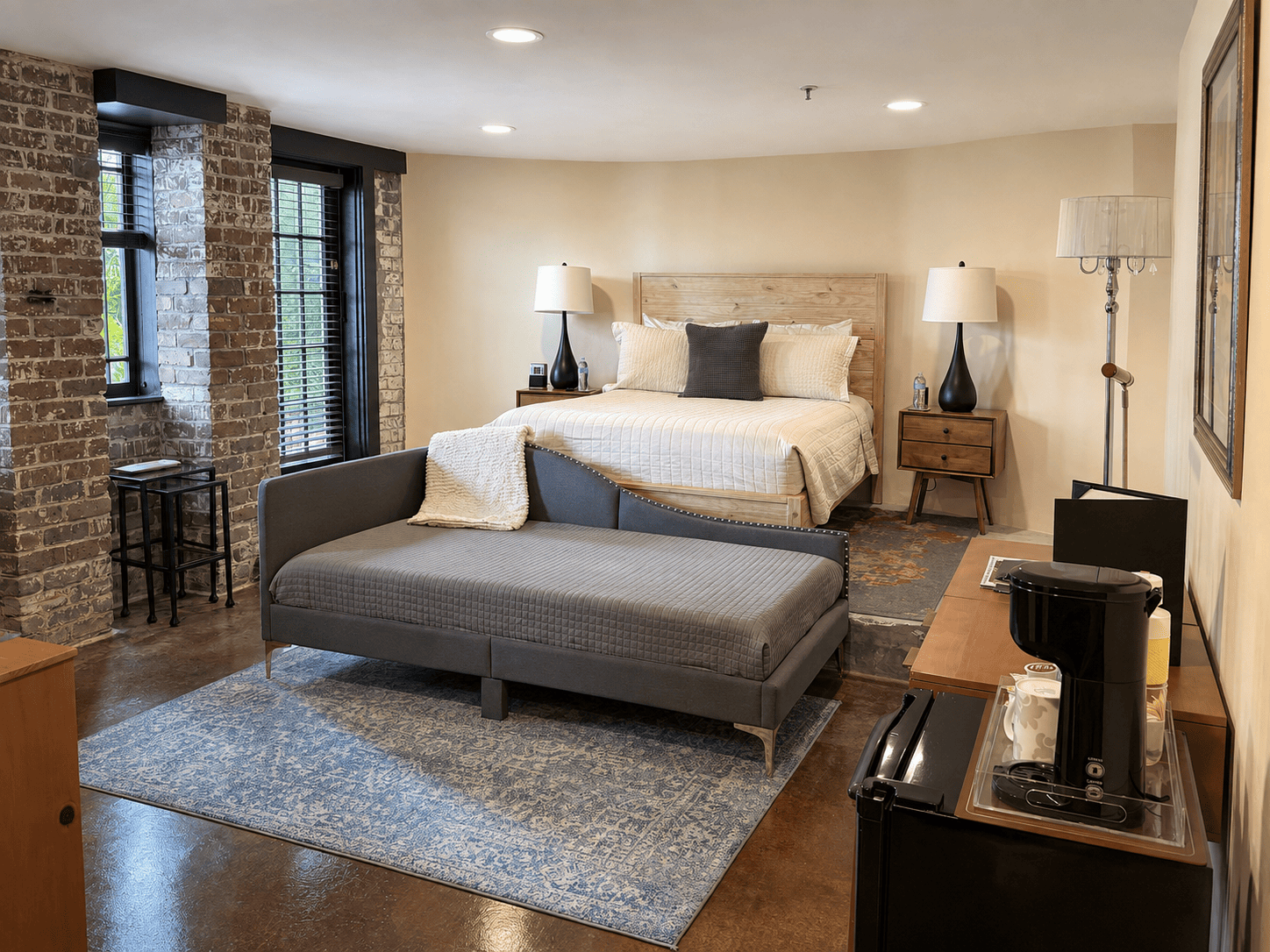 The Oak Room — queen bed with wooden headboard, grey daybed, exposed brick wall, and coffee station